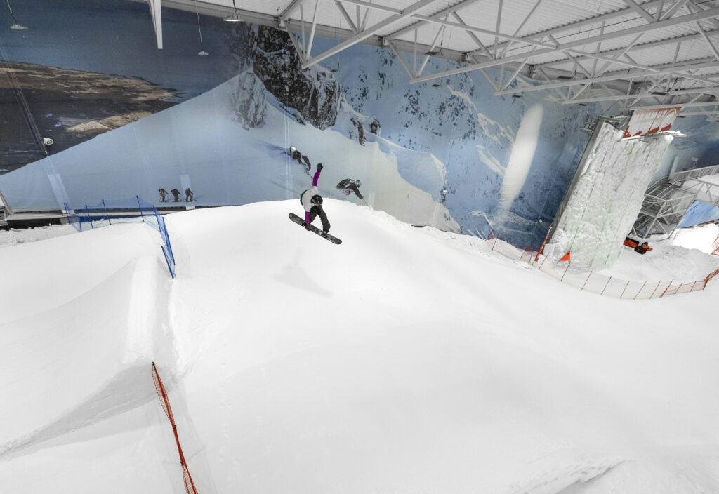 Person står på snowboard i innendørs SNØ-anlegg.